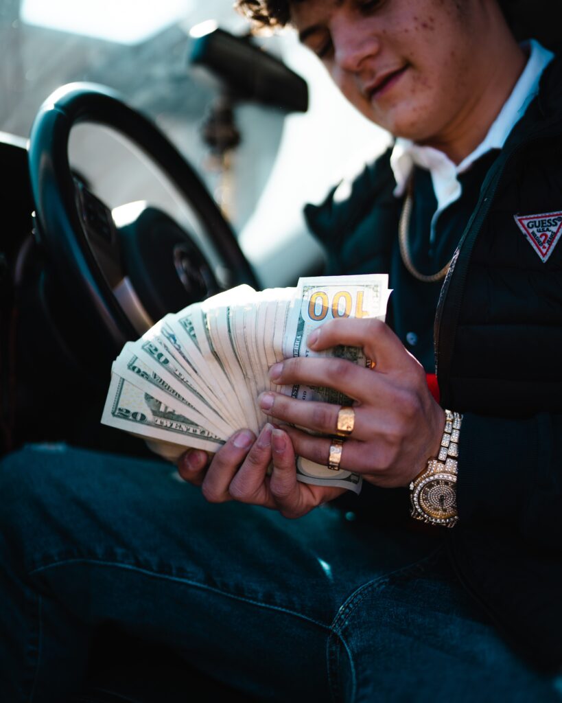 man holding and counting dollar bills whilst sat in his car